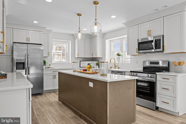 kitchen featuring appliances with stainless steel finishes, decorative light fixtures, white cabinetry, a center island, and light hardwood / wood-style flooring