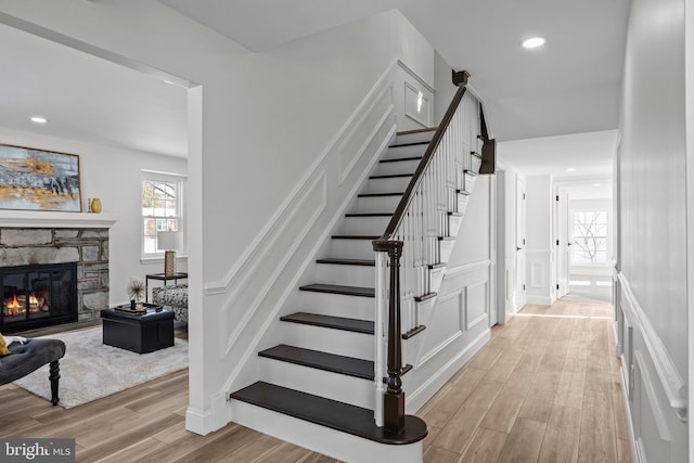 staircase with a stone fireplace and hardwood / wood-style floors