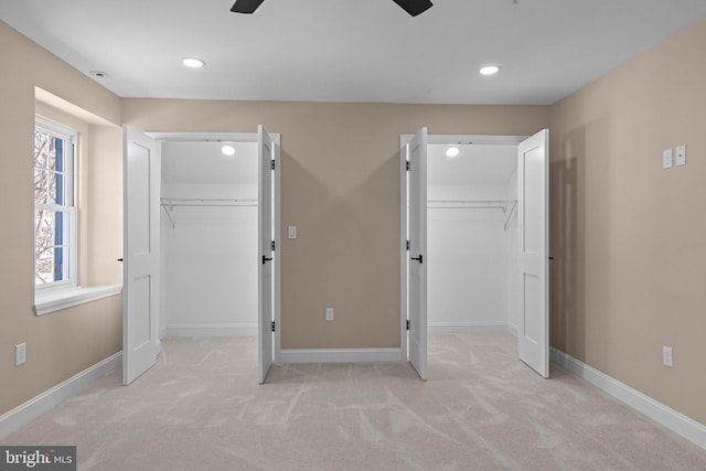 unfurnished bedroom featuring multiple windows, a walk in closet, light colored carpet, and ceiling fan