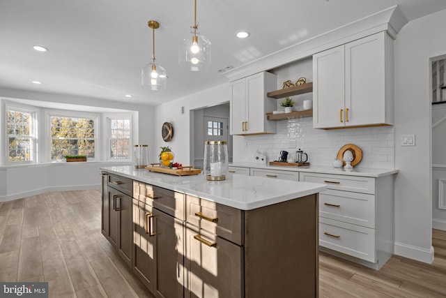 kitchen with pendant lighting, white cabinets, a center island, light stone countertops, and light hardwood / wood-style flooring