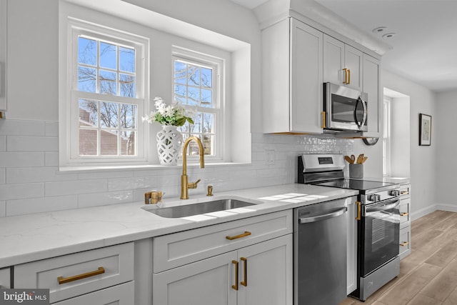 kitchen with sink, light stone counters, appliances with stainless steel finishes, a wealth of natural light, and light hardwood / wood-style floors