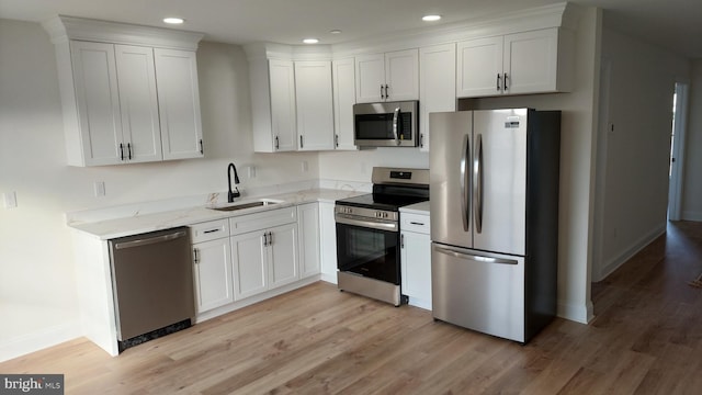 kitchen with appliances with stainless steel finishes, light stone counters, sink, light hardwood / wood-style flooring, and white cabinetry