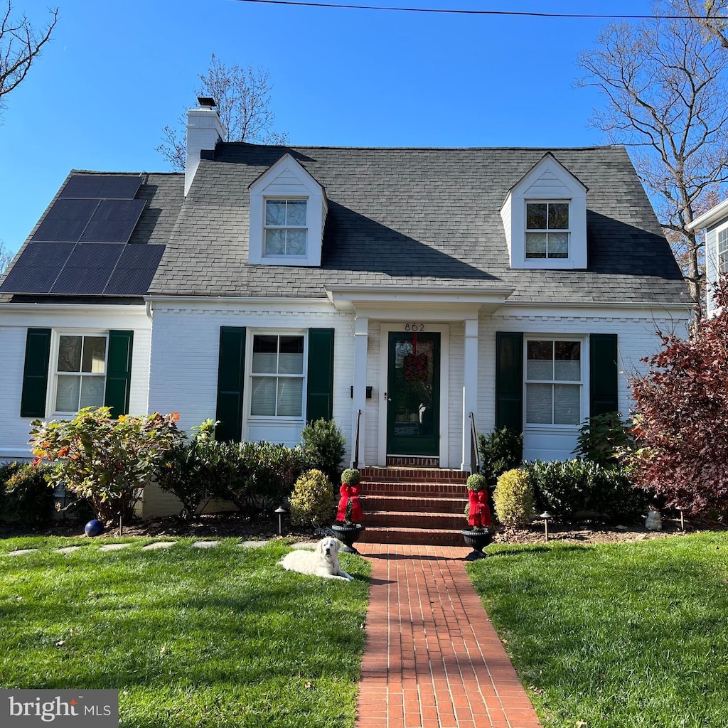 cape cod house featuring solar panels and a front yard