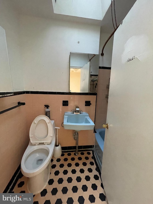 full bathroom with shower / tub combination, sink, a skylight, toilet, and tile walls