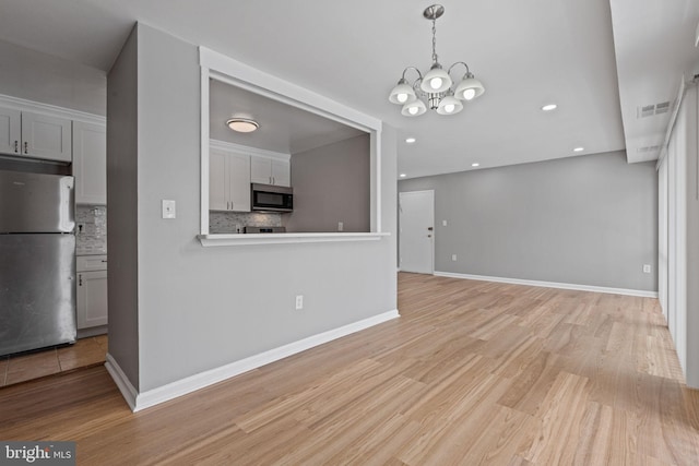 kitchen featuring decorative backsplash, appliances with stainless steel finishes, a chandelier, light hardwood / wood-style floors, and hanging light fixtures