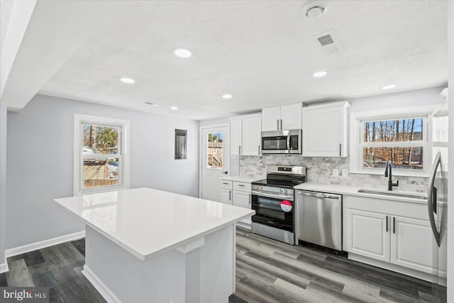 kitchen featuring appliances with stainless steel finishes, sink, tasteful backsplash, white cabinetry, and a center island