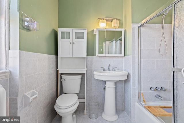 bathroom with a wainscoted wall, tile walls, toilet, combined bath / shower with glass door, and tile patterned floors