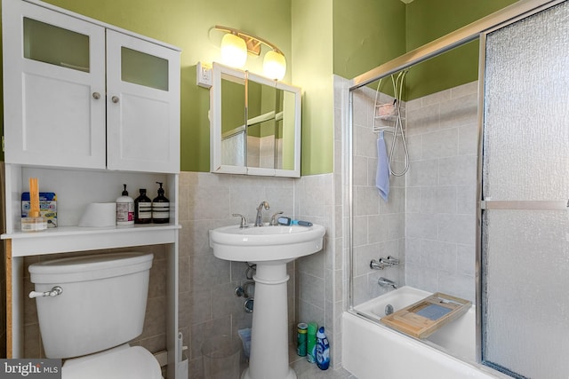 bathroom featuring tile walls, toilet, shower / bath combination with glass door, and wainscoting