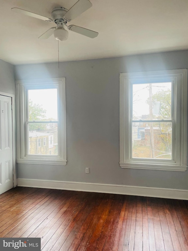 empty room with ceiling fan, a healthy amount of sunlight, and dark hardwood / wood-style floors