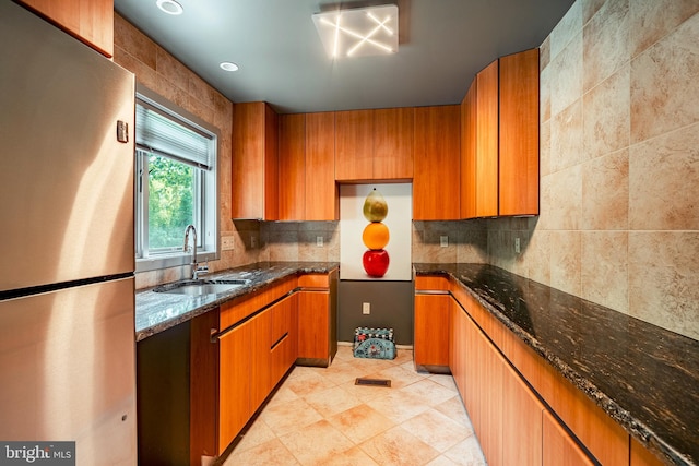 kitchen with backsplash, dark stone counters, sink, light tile patterned floors, and stainless steel refrigerator