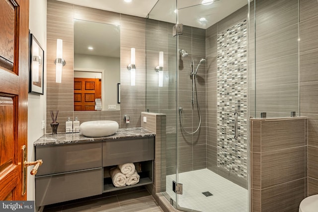 bathroom featuring a shower with door, vanity, and tile walls