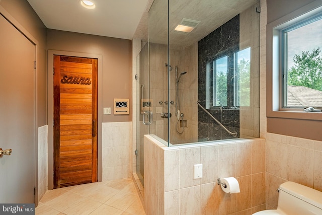 bathroom featuring tile patterned flooring, toilet, walk in shower, and tile walls