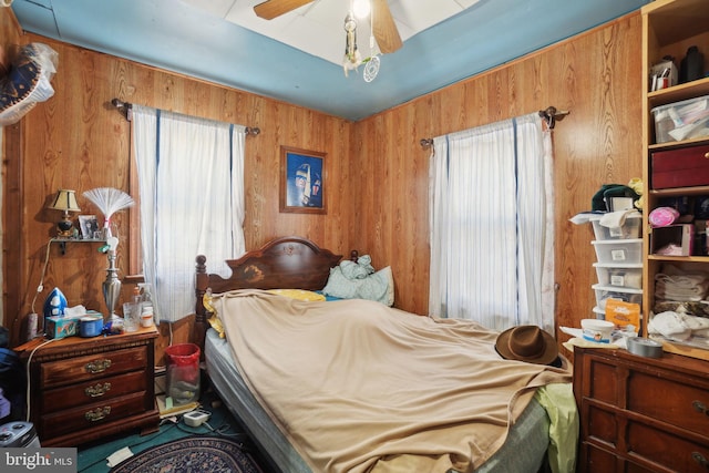 bedroom featuring wooden walls, ceiling fan, and multiple windows