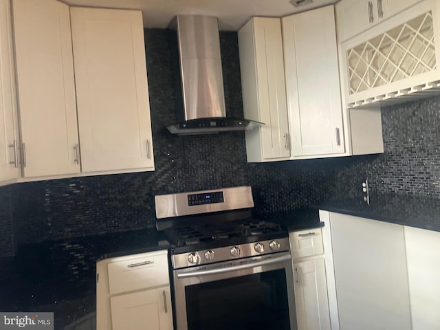 kitchen featuring stainless steel range with gas cooktop, white cabinetry, wall chimney range hood, and backsplash