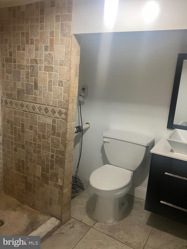 bathroom with a tile shower, tile patterned flooring, vanity, and toilet