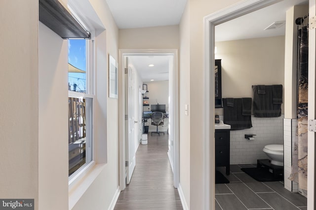 hallway featuring dark tile patterned floors and tile walls