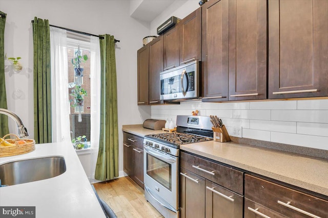 kitchen with light hardwood / wood-style floors, decorative backsplash, dark brown cabinetry, appliances with stainless steel finishes, and sink