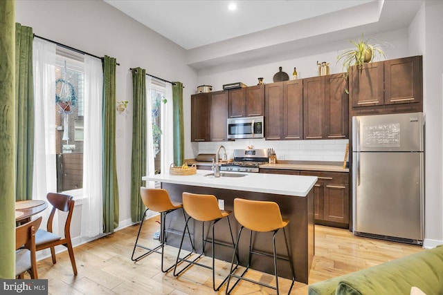 kitchen with light hardwood / wood-style flooring, a kitchen bar, a kitchen island with sink, appliances with stainless steel finishes, and sink