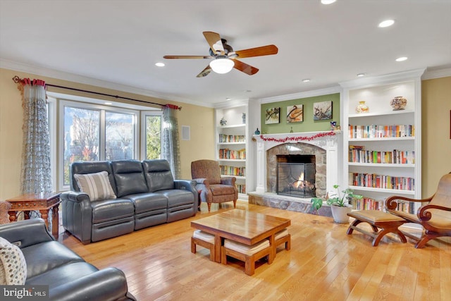 living room with a fireplace, ornamental molding, built in shelves, and light hardwood / wood-style flooring