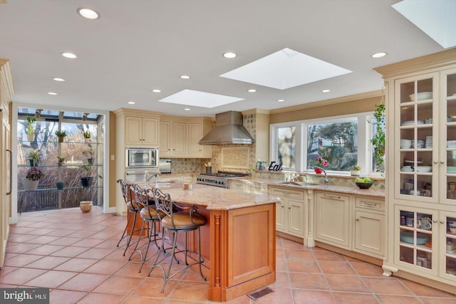 kitchen with stove, stainless steel microwave, cream cabinetry, a kitchen island, and wall chimney exhaust hood