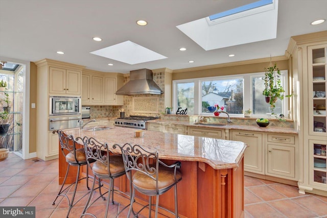 kitchen with cream cabinetry, wall chimney exhaust hood, stainless steel microwave, a kitchen island, and sink