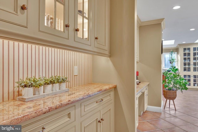 bar featuring light tile patterned flooring, cream cabinetry, crown molding, and light stone countertops