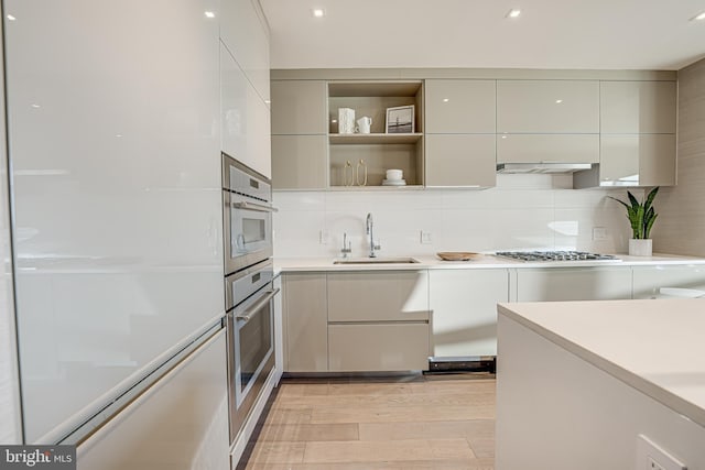 kitchen with decorative backsplash, appliances with stainless steel finishes, light wood-type flooring, ventilation hood, and sink