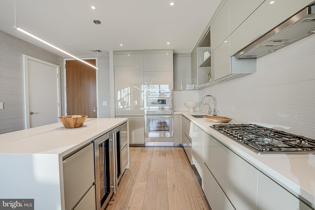 kitchen featuring sink, stainless steel appliances, wine cooler, decorative light fixtures, and exhaust hood