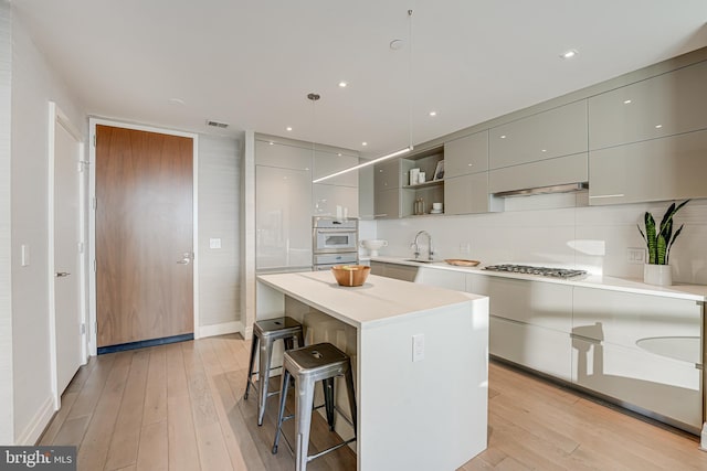 kitchen featuring stainless steel gas stovetop, light hardwood / wood-style flooring, gray cabinets, a kitchen island, and a breakfast bar area