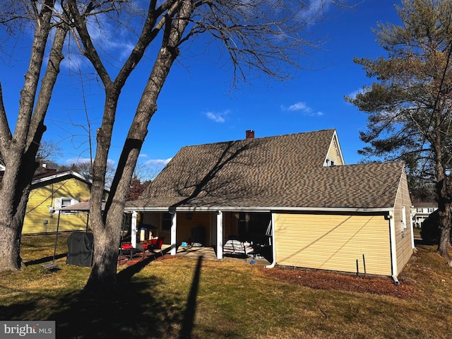 rear view of house featuring roof with shingles, a yard, and a chimney