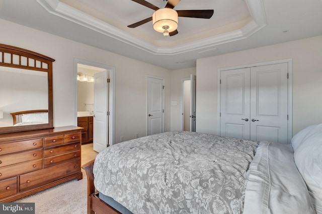 carpeted bedroom with ensuite bath, a tray ceiling, ceiling fan, crown molding, and a closet