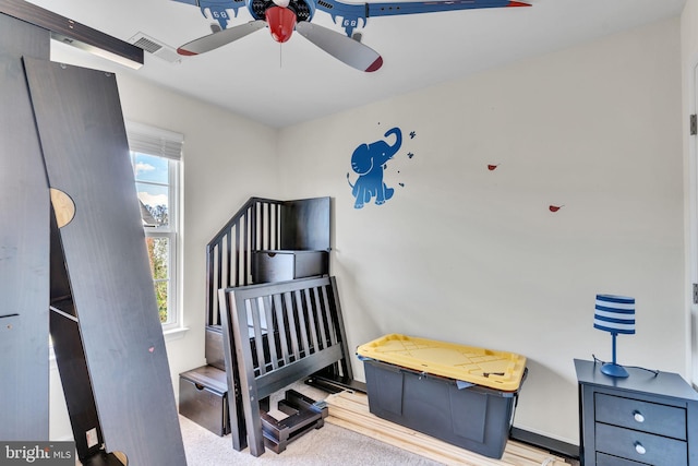 carpeted bedroom with ceiling fan and a nursery area