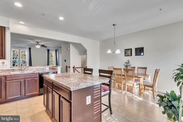 kitchen featuring ceiling fan with notable chandelier, sink, decorative light fixtures, a kitchen island, and dishwashing machine