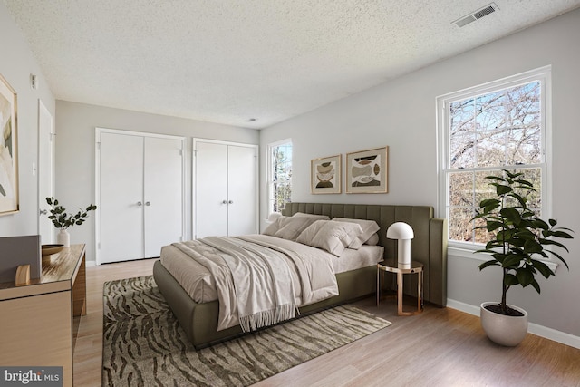 bedroom with multiple closets, light hardwood / wood-style floors, and a textured ceiling