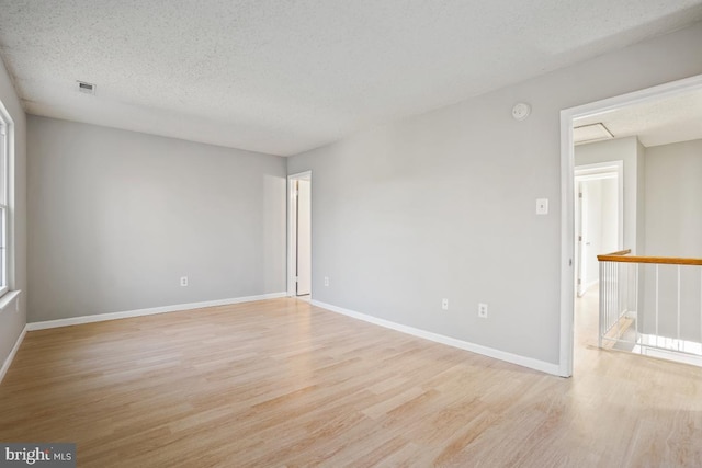 empty room with light wood-type flooring and a textured ceiling