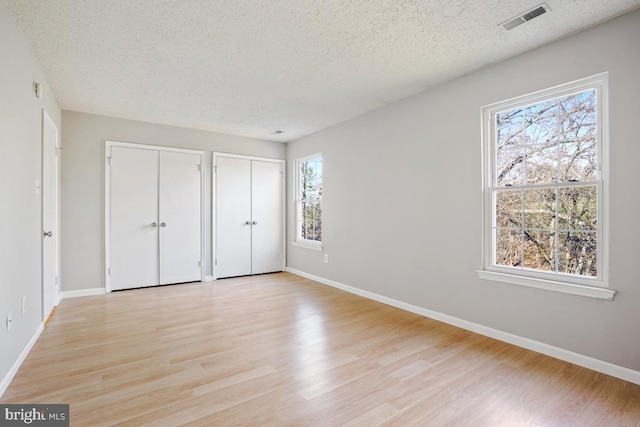 unfurnished bedroom featuring a textured ceiling, light hardwood / wood-style flooring, and multiple closets