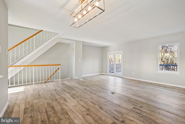 unfurnished living room featuring french doors, hardwood / wood-style floors, a textured ceiling, and plenty of natural light