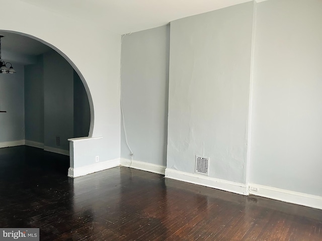 spare room featuring a chandelier and dark wood-type flooring