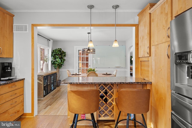 kitchen featuring a kitchen breakfast bar, stainless steel fridge with ice dispenser, dark stone counters, pendant lighting, and light hardwood / wood-style floors