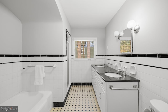 bathroom with a bathtub, vanity, tile walls, and toilet