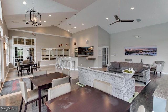 dining area with hardwood / wood-style flooring, high vaulted ceiling, and ceiling fan with notable chandelier