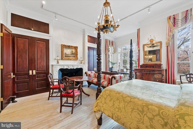 bedroom with light wood-type flooring, rail lighting, crown molding, and a notable chandelier