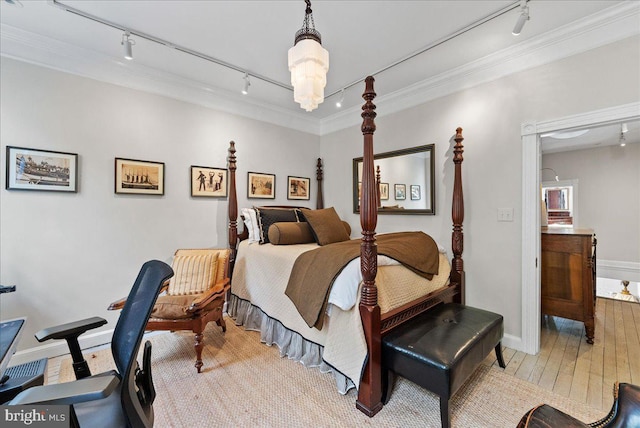 bedroom with crown molding, light hardwood / wood-style floors, track lighting, and an inviting chandelier