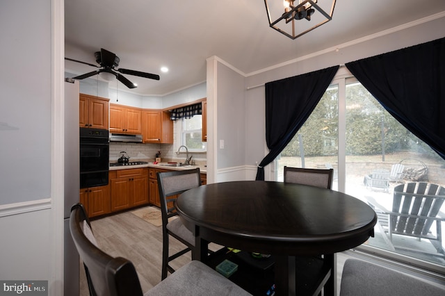 dining space featuring sink, light hardwood / wood-style flooring, crown molding, and ceiling fan with notable chandelier