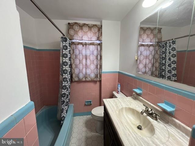 full bathroom featuring tile patterned flooring, shower / bath combination with curtain, toilet, vanity, and tile walls