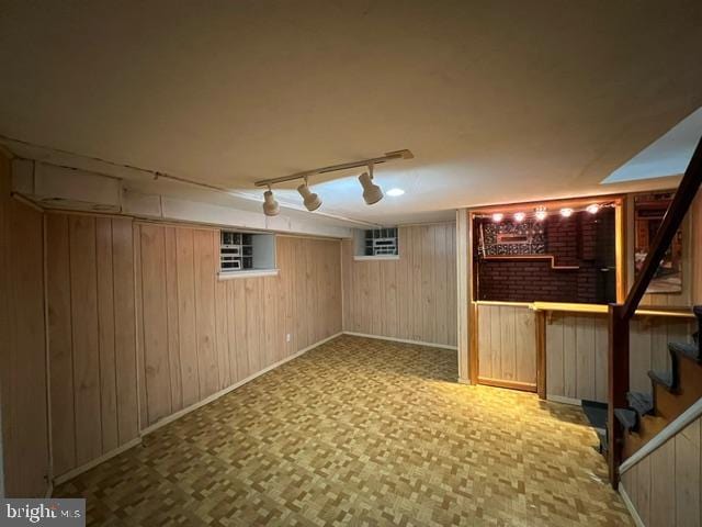 basement with rail lighting and wood walls