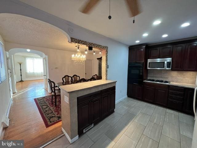 kitchen with ceiling fan with notable chandelier, hanging light fixtures, decorative backsplash, appliances with stainless steel finishes, and dark brown cabinetry