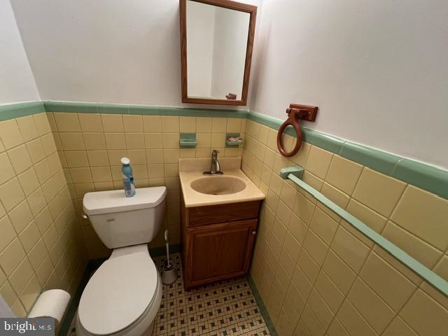 bathroom featuring tile patterned floors, vanity, toilet, and tile walls