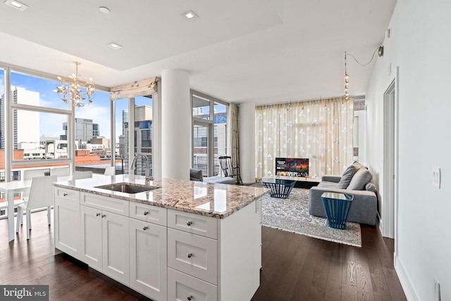 kitchen with white cabinets, sink, light stone counters, and an island with sink