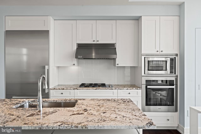 kitchen featuring built in appliances, white cabinets, and range hood